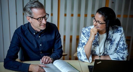 En man och en kvinna sitter bredvid varandra vid ett bord och diskuterar innehållet i en bok.