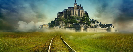 A city surrounded by a wall with a castle on a hill visible at the end of a pair of railway tracks.
