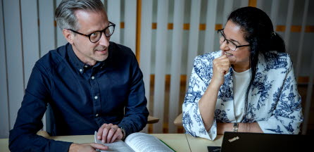 En man och en kvinna sitter bredvid varandra vid ett bord och diskuterar innehållet i en bok.