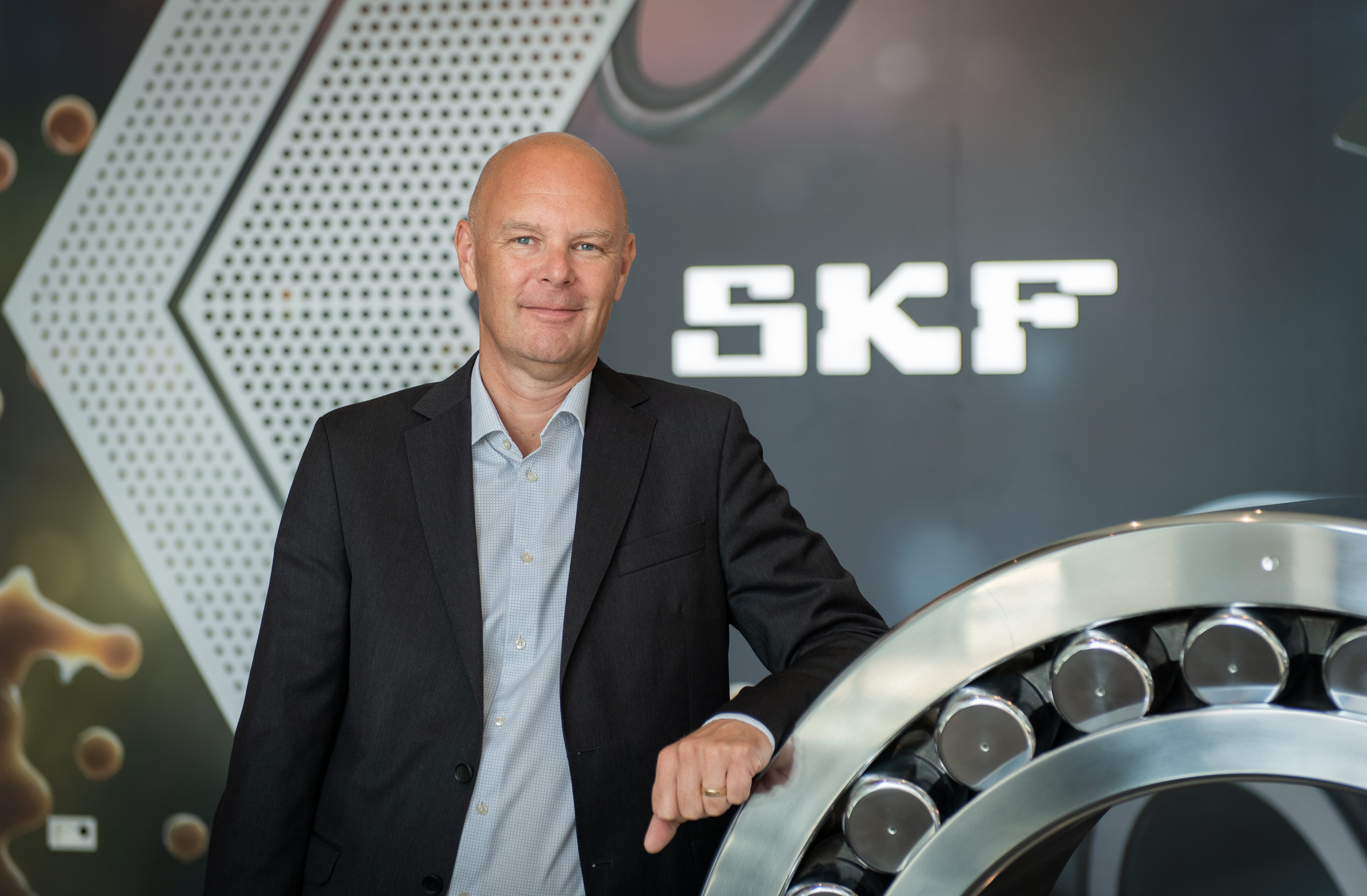 Johan Bravert at SKF is dressed in a suit, in front of a ball bearing, where the SKF logo can be seen in the background.