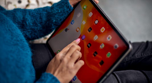 Woman in a blue knitted sweater is seated and using an iPad.