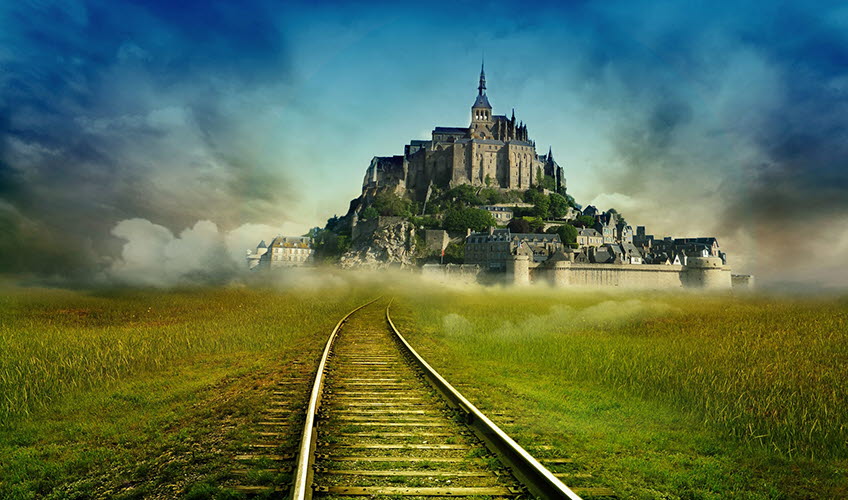 En tågräls omgiven av grönt gräs och ett slott i horisonten
