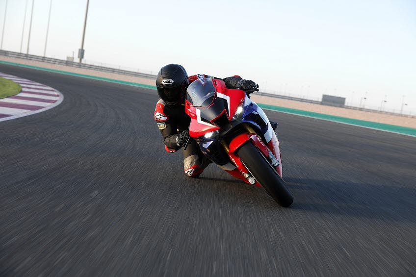En motorcyklist med röd, vit och blå motocykel ligger ner i en kurva när han kör på en bana.