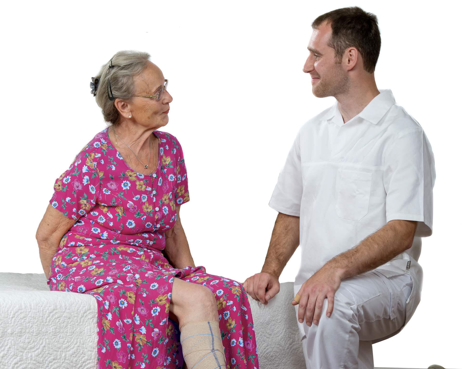 A woman sitting on a bed and she has a bandage around her leg. A doctor sits next to her.