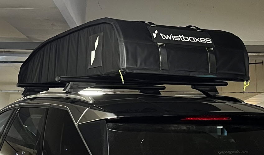 En svart takbox i kanvas med texten Twistboxes är monterad på en svart bil.
