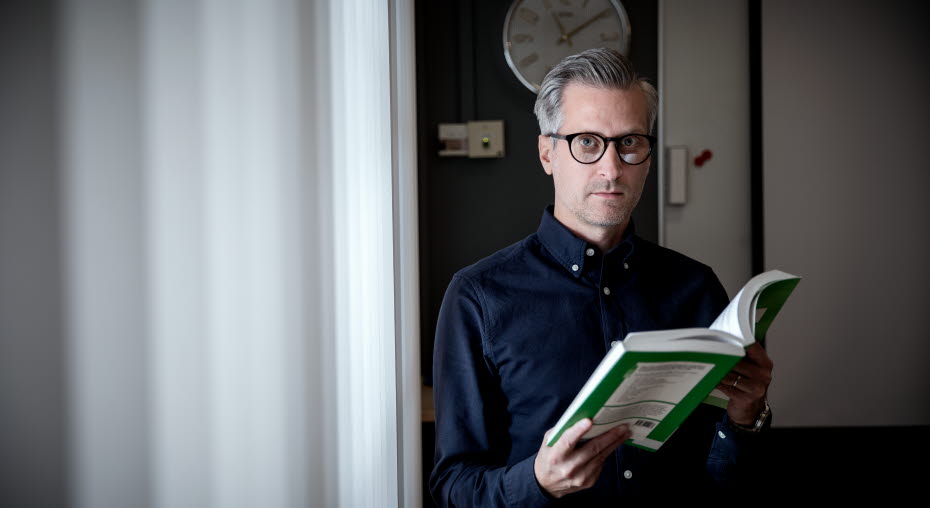 En man står med en uppslagen bok i handen.