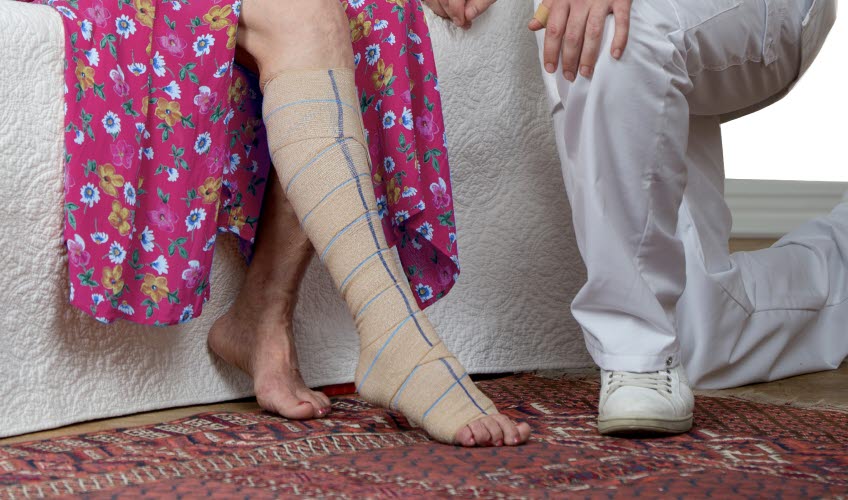 Kvinna i rosa klänning sitter ner med ett synligt bandage över ena benet.