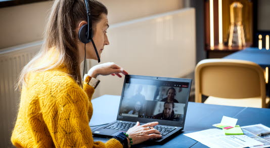 Kvinna med hörlurar deltar i teamsmöte på laptop.