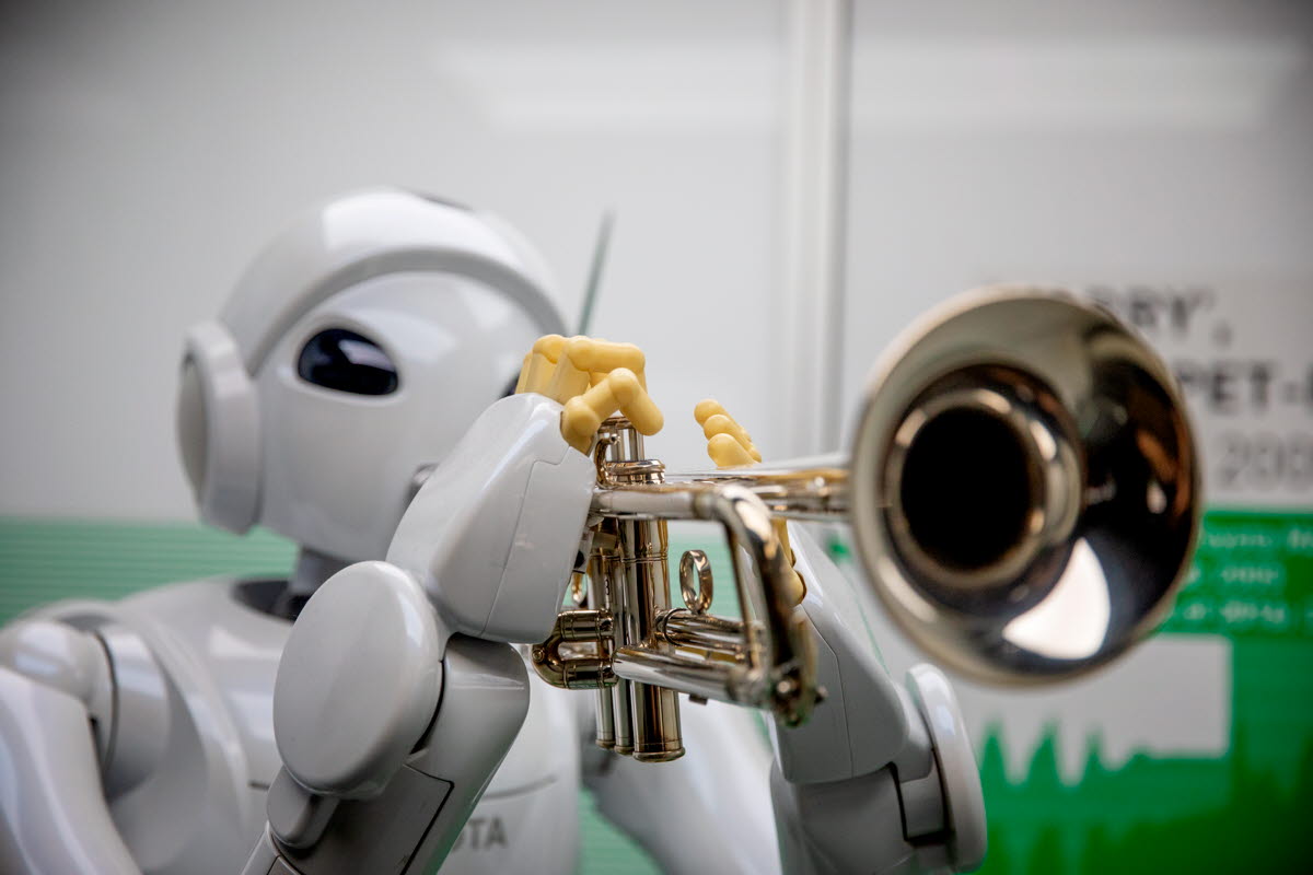 A white robot plays a trumpet.