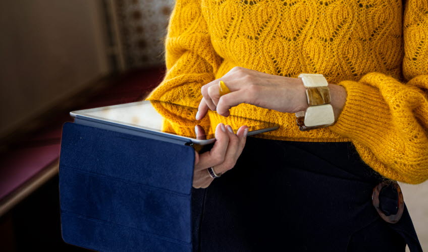 Kvinna i gul stickad tröja använder en IPad